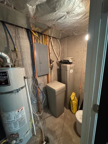 Utility area featuring a water heater, electrical panel, and water conditioning system