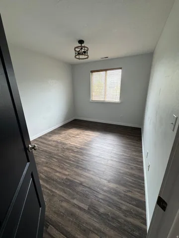 Spacious room featuring wood-finish flooring, a window with horizontal blinds, and a modern ceiling-mounted light fixture