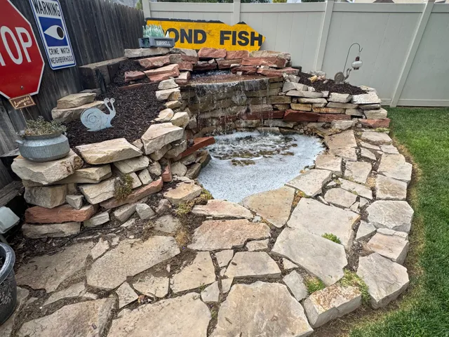 Stone water feature with a waterfall, flagstone patio, and a wood privacy fence