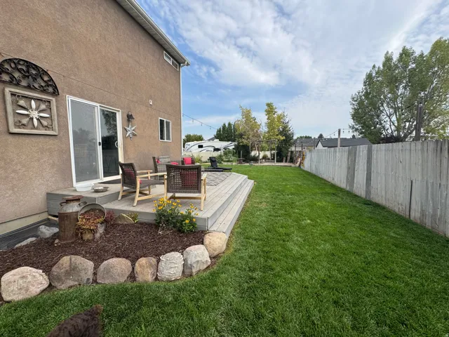 Expansive backyard featuring a manicured lawn, a large wood-finish deck, rock-lined landscaping beds, and a full privacy fence