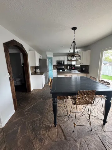 Kitchen featuring white cabinetry, stone countertops, stainless steel appliances, and a central island with an overhead light fixture