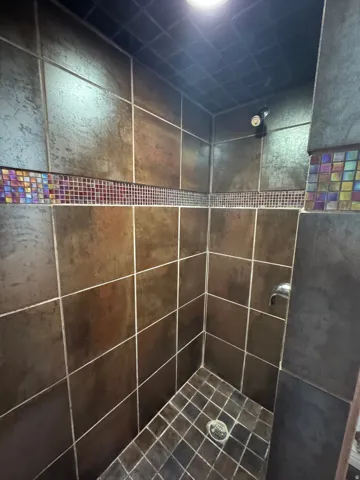 Tiled shower enclosure featuring a mosaic accent band, square floor tiles, and a wall-mounted shower head