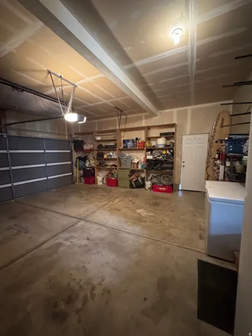 Concrete flooring with a white interior door, exposed ceiling joists, and overhead lighting