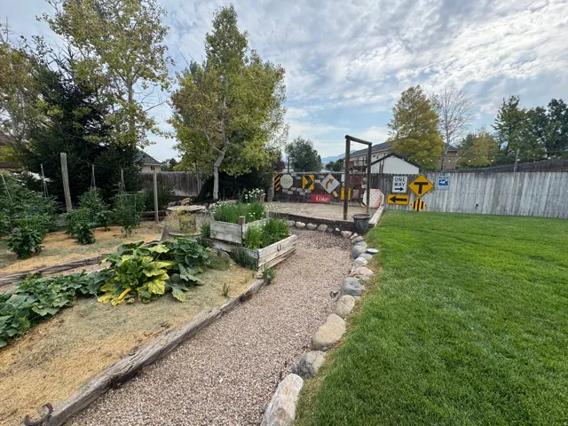 Manicured lawn, gravel pathway, raised garden beds, mature trees, and a wooden privacy fence