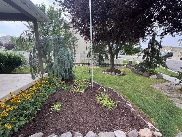Manicured front yard with mature trees, established flower beds, and a stone-edged garden