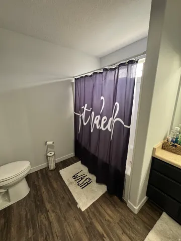 Bathroom featuring wood-finish flooring, a toilet, a full bathtub with a shower, and a vanity with a light-colored countertop