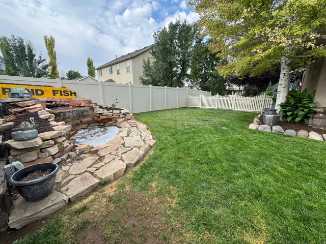 Expansive lawn area with a multi-level stone water feature, perimeter fencing, and mature trees