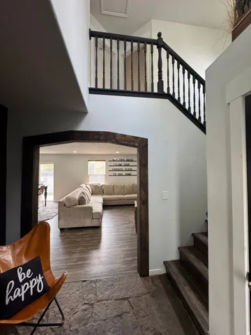 Two-story entry featuring dark wood-finish stairs and banister, leading to a spacious living area with wood-finish flooring and a wood-beamed arched doorway