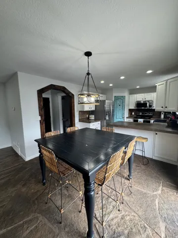 Open-concept kitchen and dining area featuring stone flooring, a decorative arched doorway, recessed lighting, and a kitchen with white cabinetry and stainless steel appliances