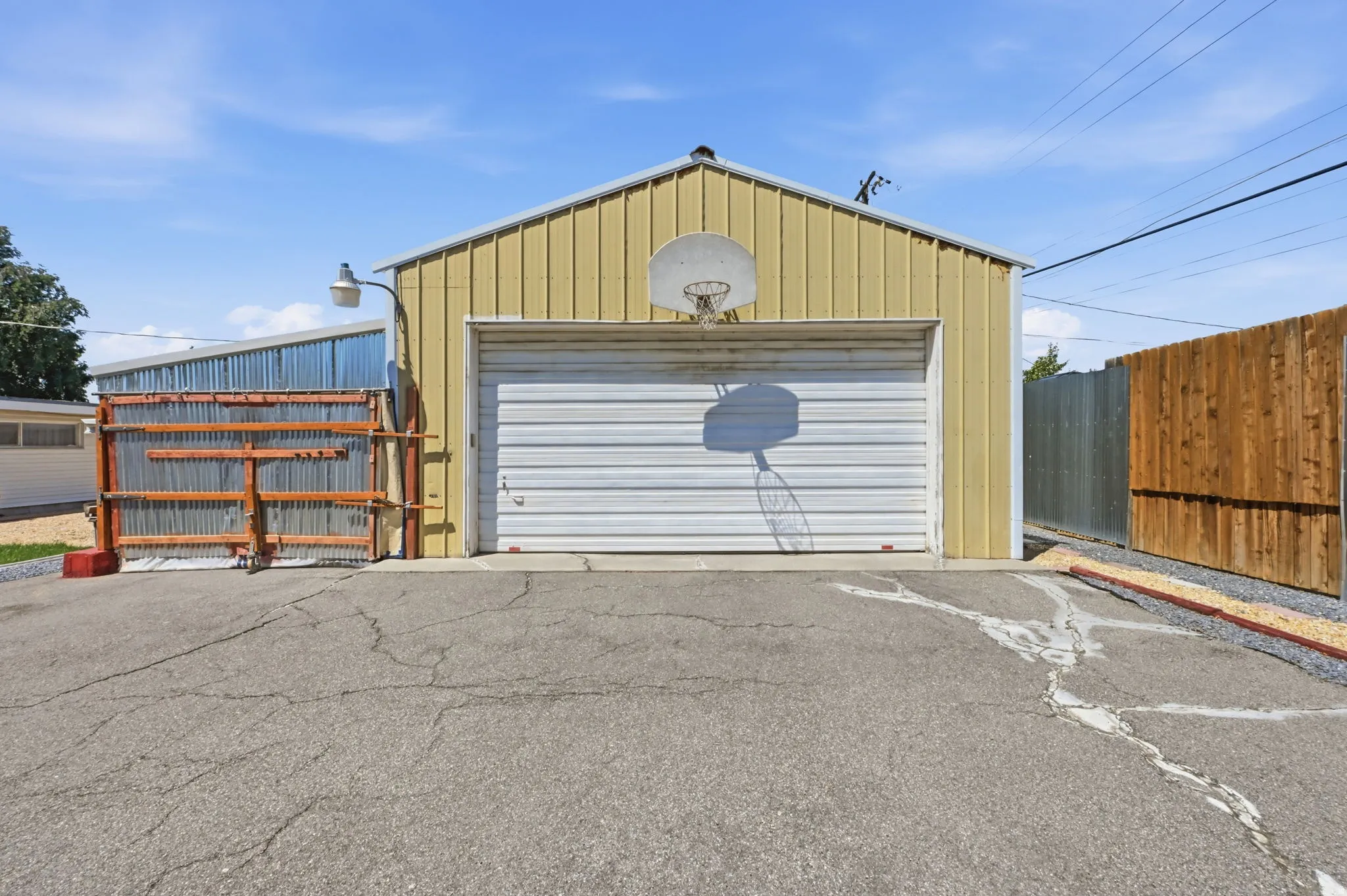 Metal-sided outbuilding with an attached garage door, overhead light fixture, and an adjacent wood privacy fence