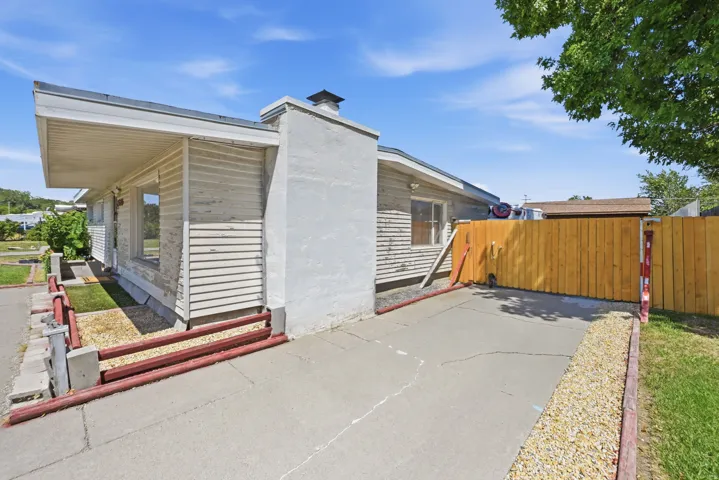 Concrete driveway, wood fencing, horizontal siding, exterior chimney, and exposed aggregate landscaping
