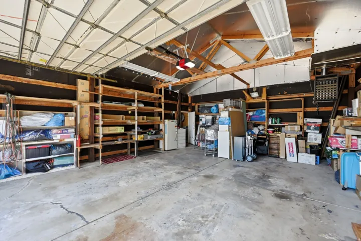 Concrete flooring, exposed wood beam ceiling, built-in shelving, overhead lighting, and wall-mounted heater
