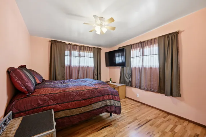 Wood-finish flooring with dual windows, a ceiling fan, and a wall-mounted display