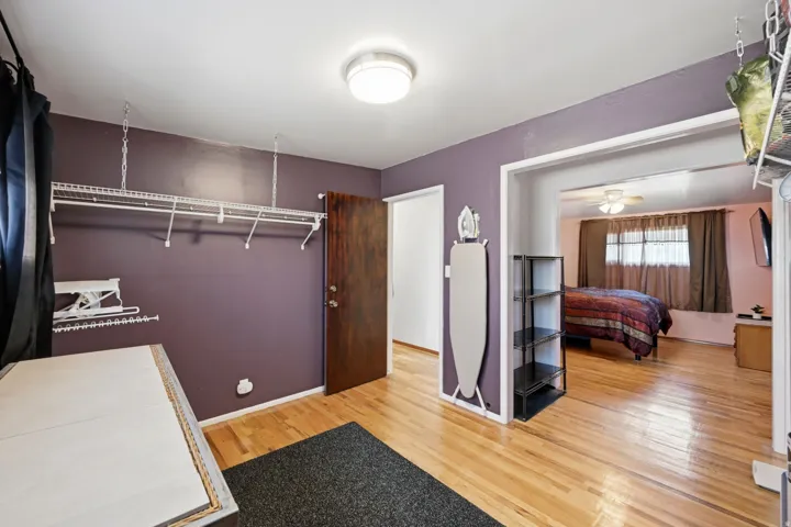 Hardwood flooring throughout, recessed ceiling light, built-in shelving, white trim, and a dark-finish door