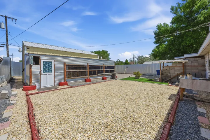 Expansive gravel area with red-painted timber borders, accompanied by a corrugated metal-sided outbuilding featuring a white door and window