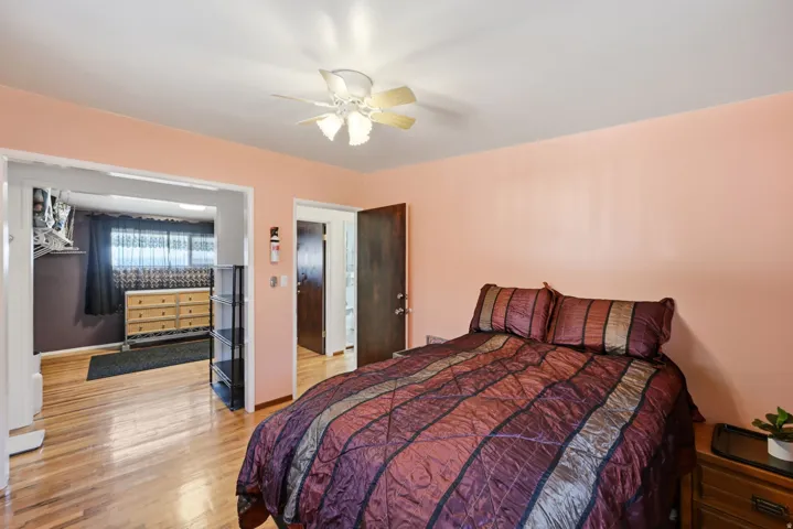 Spacious primary bedroom featuring warm peachy-toned walls, wood-finish flooring, and a ceiling fan with integrated lighting