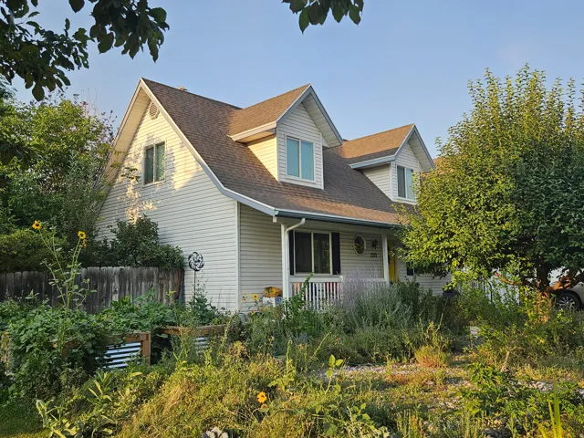 White siding exterior with multiple dormer windows, a covered front porch, and a brown shingle roof