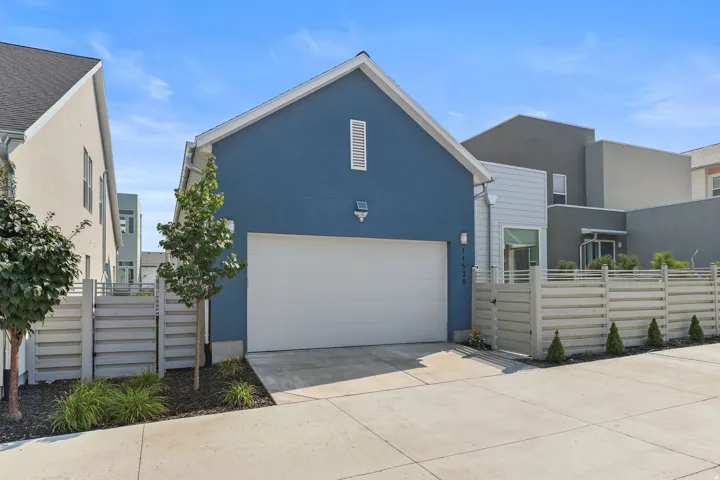 Blue stucco exterior with a white garage door, featuring an adjacent slatted fence and concrete driveway