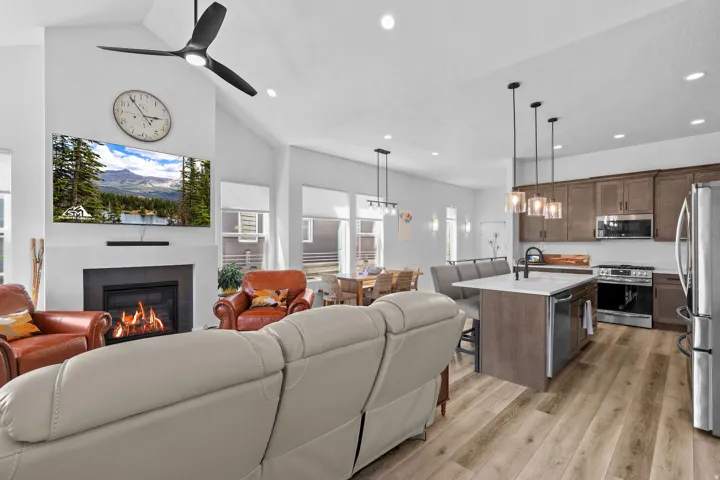 Vaulted ceiling, contemporary fireplace, wood-finish flooring, kitchen island with seating, and integrated stainless steel appliances
