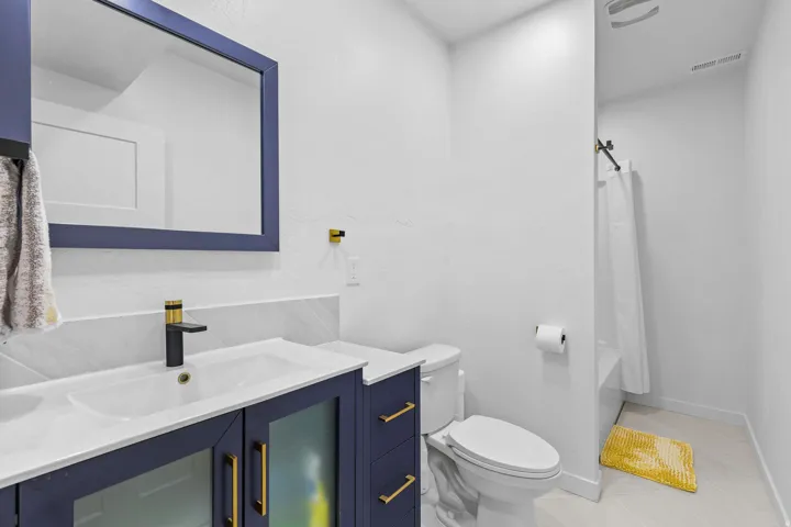 Vanity with a white countertop and integrated sink, matte black and gold-tone faucet, framed mirror, and built-in shower with a white tiled surround