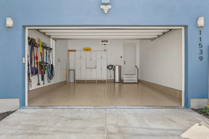 Spacious garage with an epoxy-coated floor, built-in white cabinetry, and a service door
