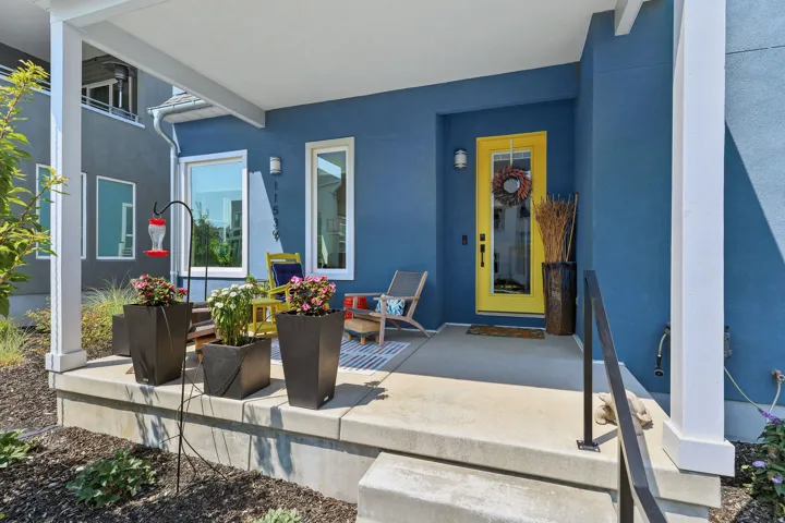 Covered concrete porch with a bright yellow entry door and white window trim