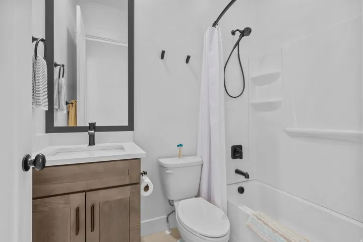 Bathroom with wood-finish vanity, white countertop with integrated sink, black framed mirror, and a white tub with shower