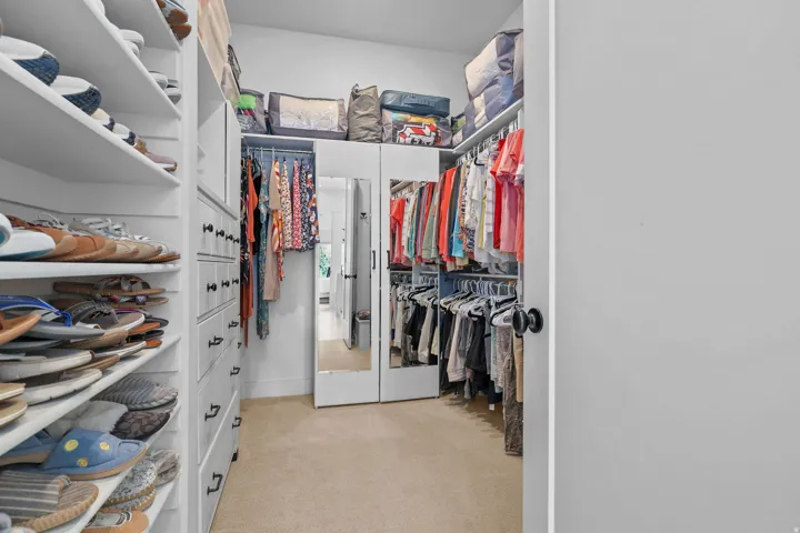 Walk-in closet featuring built-in shelving, integrated drawers with dark hardware, mirrored cabinet doors, and ample hanging space