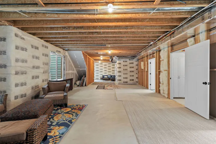 Unfinished basement with exposed wooden joists, concrete flooring, recessed window, and white paneled doors