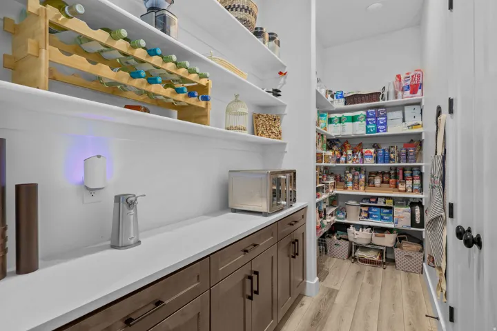 Built-in pantry shelving, wood-finish flooring, white countertops, built-in lower cabinetry, and a wine storage rack