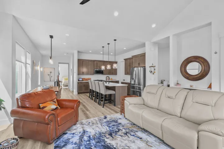 Open-concept living area with wood-finish flooring, a kitchen island with seating, pendant lighting, and stainless steel appliances