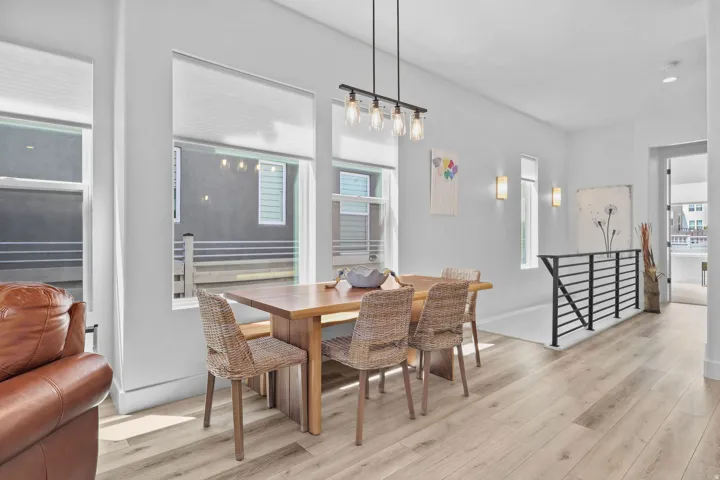 Spacious open-concept area featuring wood-finish flooring, large windows with roller shades, and a contemporary linear pendant light fixture