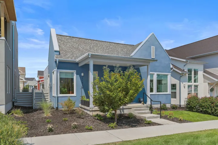 Stucco exterior with a covered porch, established landscaping, and a concrete walkway