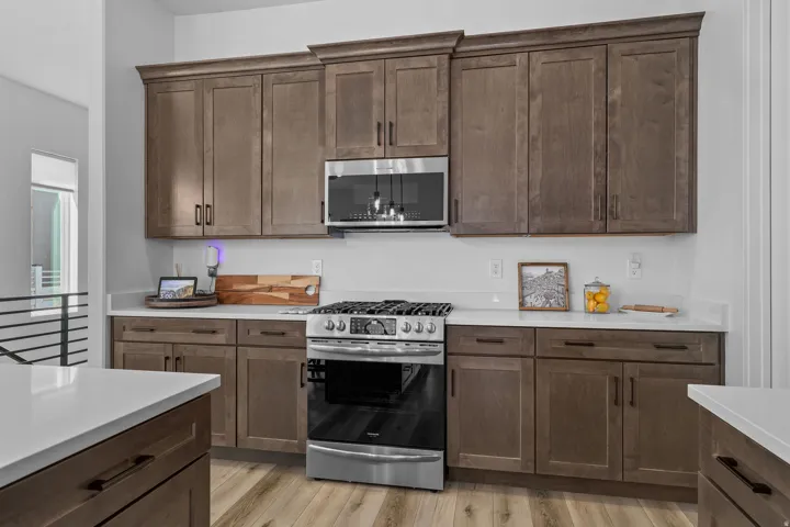 Full-height wood-finish cabinetry, stainless steel range and microwave, light-toned countertops, and wood-finish flooring