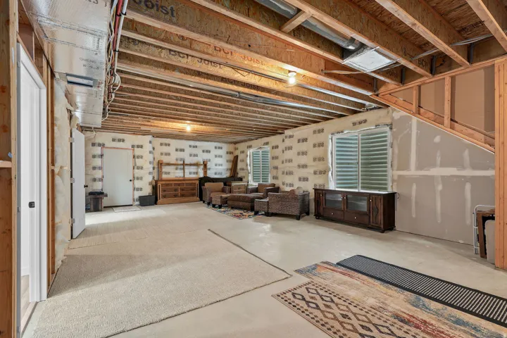 Unfinished basement with exposed ceiling joists and framing, includes two windows with horizontal blinds, and a partially framed staircase