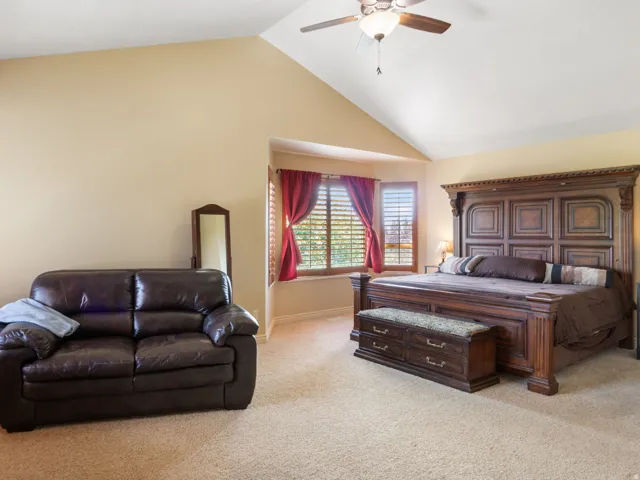 Primary Bedroom. Vaulted ceiling with ceiling fan, bay window with plantation shutters, and carpeted flooring.