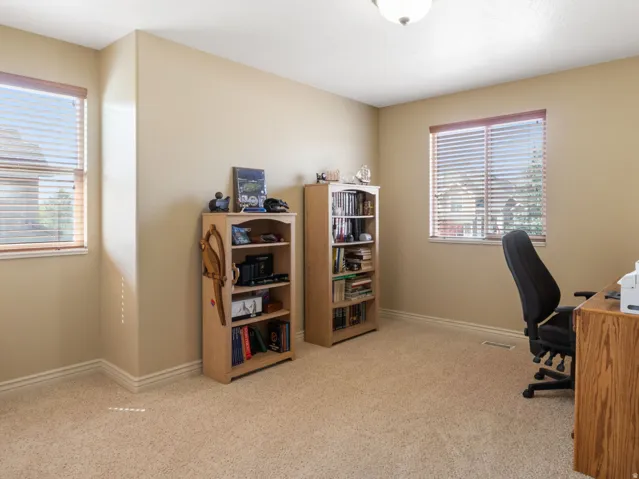Additional bedroom 2, used as home office. Spacious home office featuring abundant natural light from dual windows with plantation shutters, neutral carpet flooring, and built-in wood shelving units ideal for storage and organization