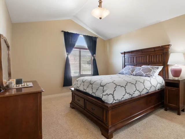 Bedroom 1. Vaulted ceiling with an attached light fixture, a window with blinds, and carpet flooring