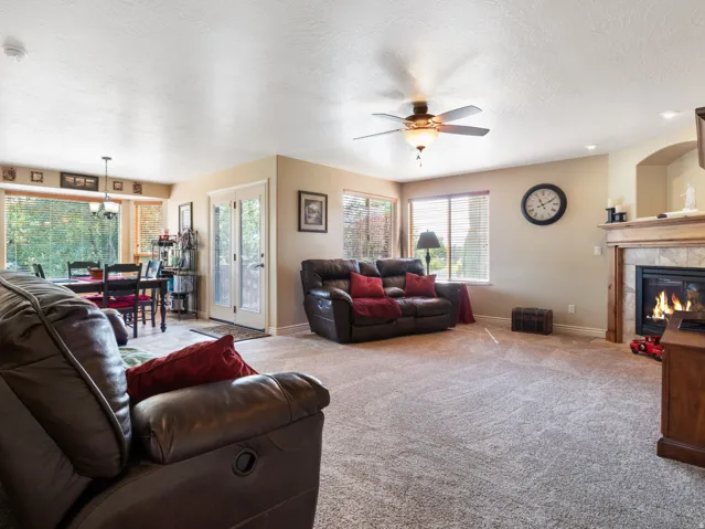 Spacious room featuring carpeting, a ceiling fan, and a fireplace with a tiled surround and wood mantel.
