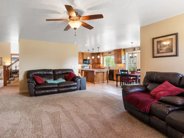 Open-concept living area featuring a ceiling fan, carpet flooring, and a kitchen with wood cabinetry, a center island, recessed and pendant lighting.