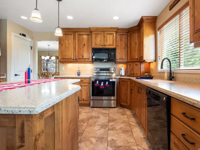 Kitchen featuring wood cabinetry, light-colored speckled countertops, a stainless steel range, and a black microwave