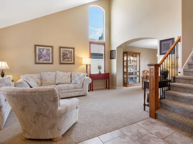 Vaulted ceiling, arched window, tiled entryway, carpeted living area, and a staircase with wood newel posts and wrought iron balusters.