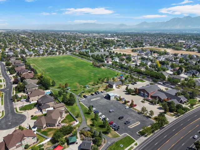 Expansive neighborhood featuring a large green park with popular splash pad, residential properties with varied rooflines, a community building with a substantial parking area, and distant mountains.