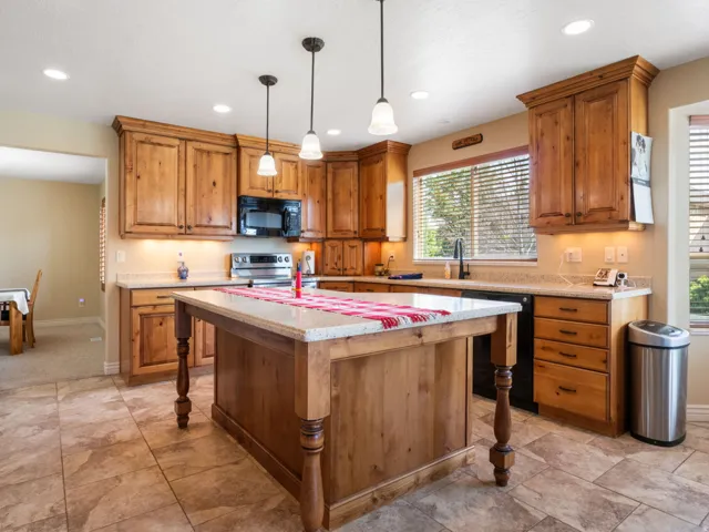Kitchen featuring wood cabinetry, stone-look countertops, a central island with pendant lighting, and tiled flooring