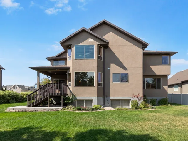 Expansive rear elevation featuring a covered deck, exterior stairs, multiple windows, and a lower-level concrete patio.