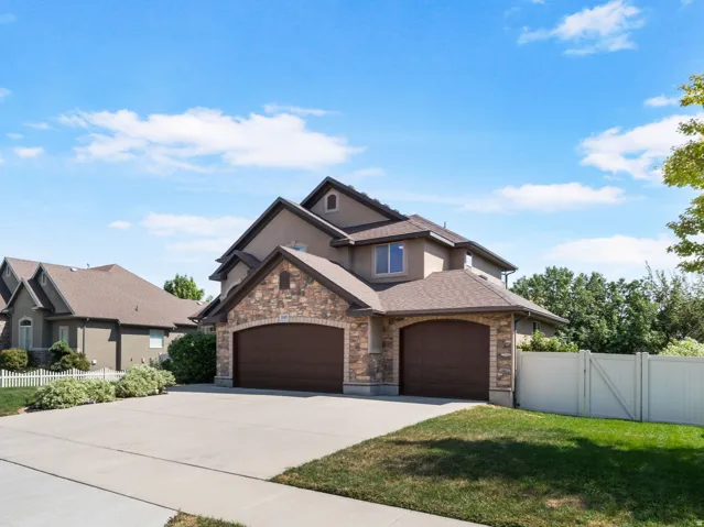 Stucco exterior with stone accents, featuring a dual-door attached garage, concrete driveway, and a white picket fence.