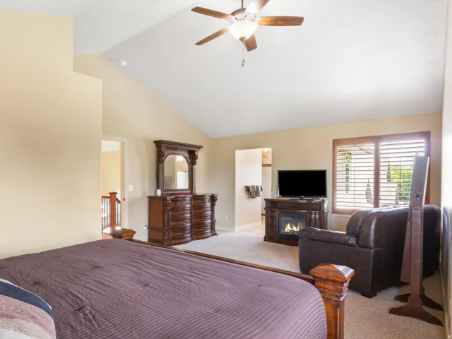 Primary Bedroom. Vaulted ceiling with a ceiling fan, window with plantation shutters, built-in fireplace, and carpeted flooring.