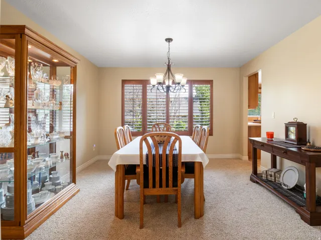 Formal Dining Room. Recessed lighting, warm-toned walls, and a chandelier illuminate a space with a window featuring wood-tone plantation shutters
