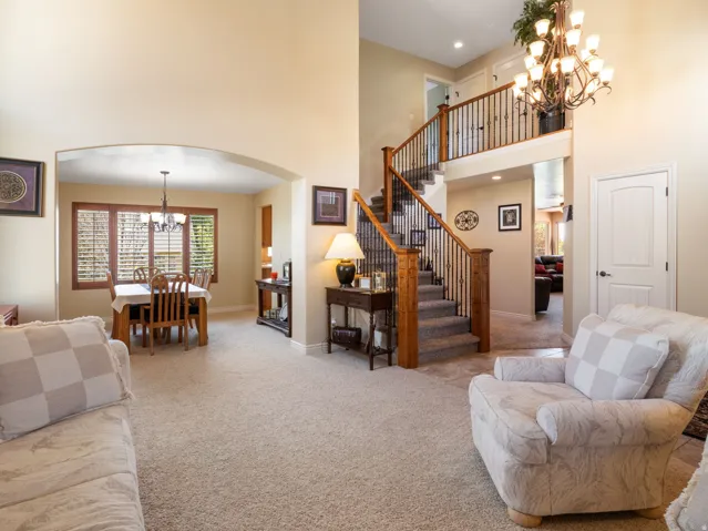 Two-story foyer with a wrought iron and wood staircase, chandelier lighting, and an arched entry to a dining space with window shutters