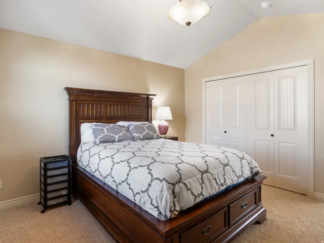 Additional bedroom 1. Vaulted ceiling, carpeted flooring, and bi-fold closet doors with black hardware